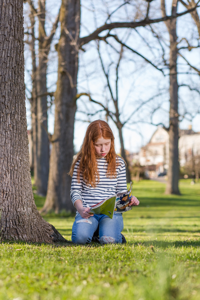 girl reads book outside under tree