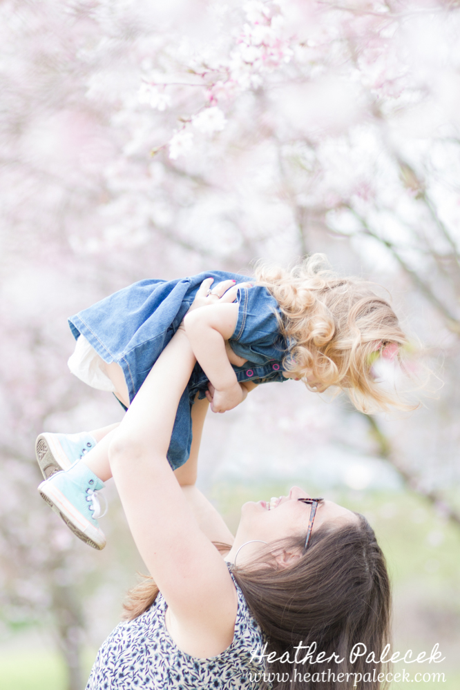 mom holds up daughter under cherry blossom tree
