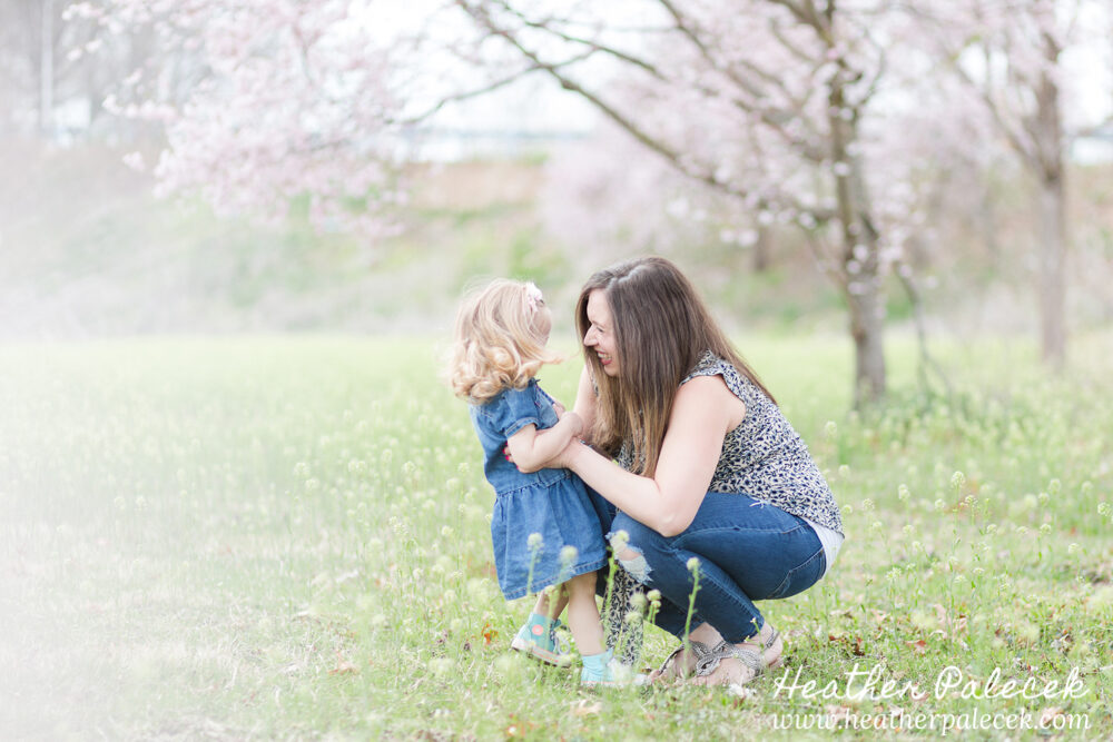 mother and daughter laugh with cherry blossom tree in background
