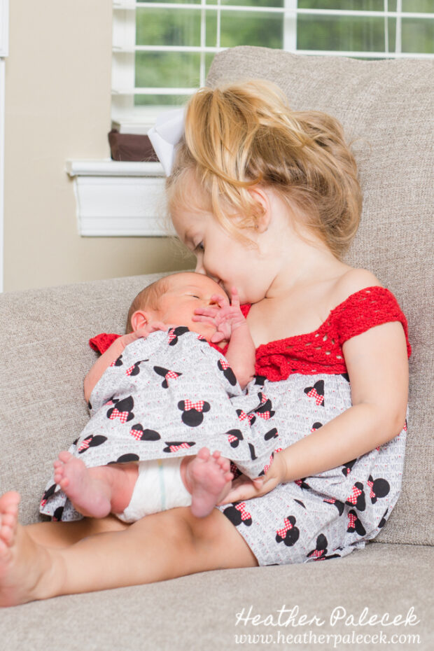 sister holding newborn in minnie mouse dress