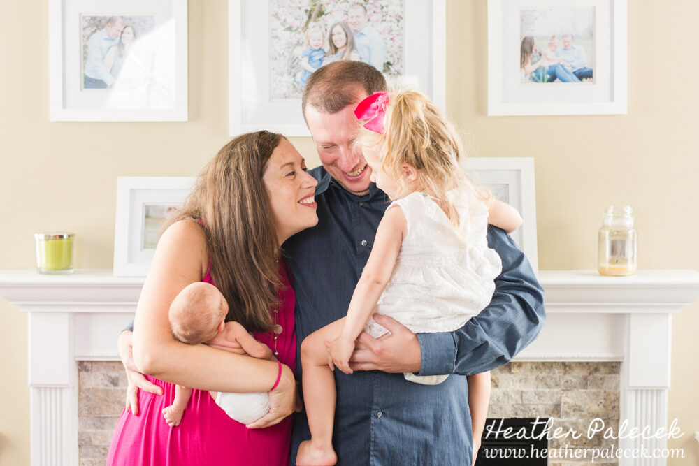 family of four pose with newborn daughter in living room