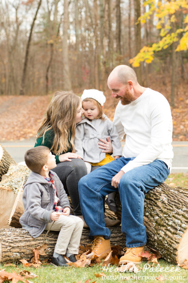 family sits on pile of logs at Fall Family Photo Shoot
