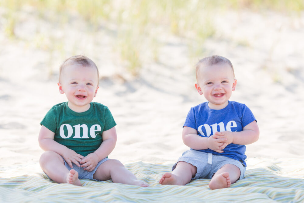 twin boys on beach in front of dunes taking one year birthday portrait